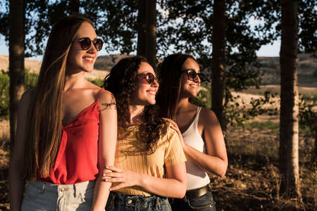 Three beautiful and diverse young women in sunglasses are in the field and smiling on a sunny day.の写真素材