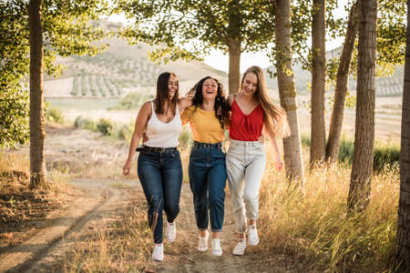Smiling young women walk holding each other through the fieldの写真素材