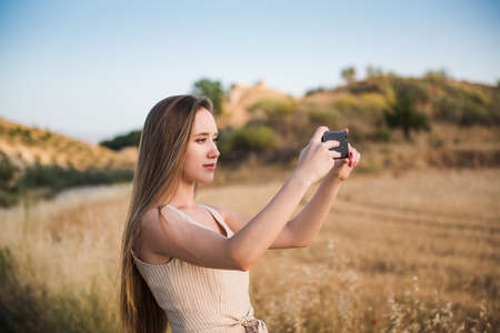 blonde young woman taking photos in the field with her mobile phone