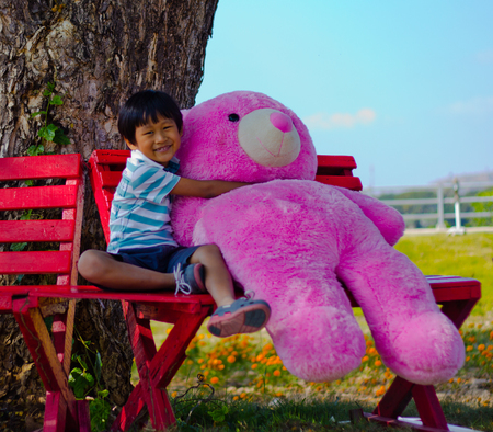 Asian boy hug a pink bear doll under treeの写真素材