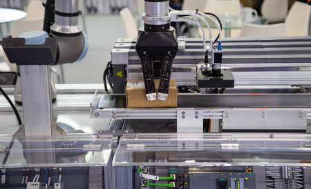 Robot arm loading carton on conveyor in manufacturing production line