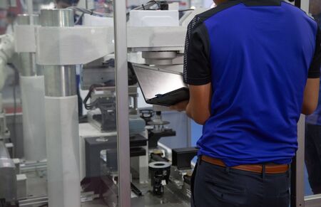 Worker using laptop to operate automation assembly robot in automotive industry