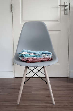 Stack of folded clean clothes on modern chair in front of the door.