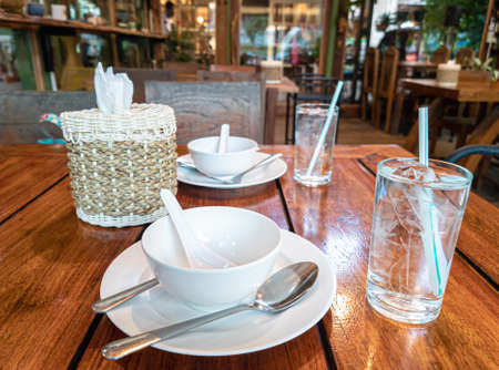 Thai restaurant setting table interior. Glasses of water with straw, plates and tissue paper on...
