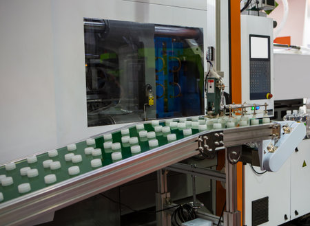 Plastic bottle caps on conveyor belt from plastic injection molding press machine. Industrial...