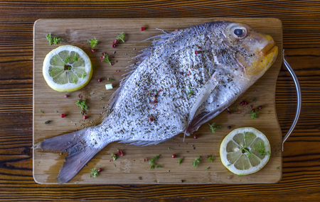 Fresh uncooked dorado or sea bream fish with lemon; herbs; pepper; and spices on wooden board