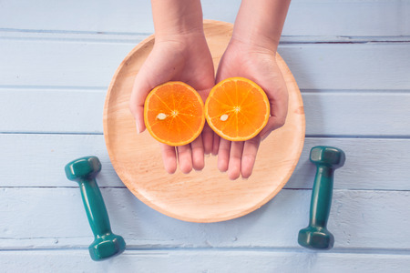 Healthy food on wood background, Female hands hold Slice of Fresh orange, with color filters, Top...