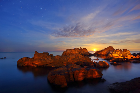 Long Exposure of stars, the moon is falling with rocks and sea in the dawnの写真素材