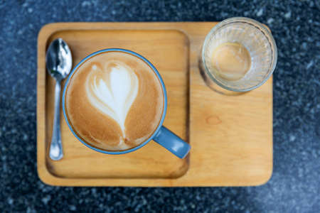 Hot of Latte coffee with heart pattern and cold water glass in a cup on wooden tray on marble table