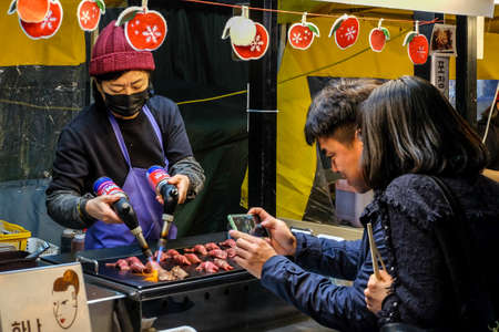 Daegu , South Korea, April 4, 2019: Tourist taking picture while chef burn a slice of wagyu beef with blowtorch for make a sushi caramelize at seomun market at nightのeditorial素材