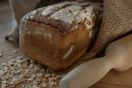 A loaf of bread on a bamboo board, sprinkled with oat flakes, in a burlap bagの写真素材