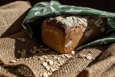 A loaf of bread on a bamboo board, sprinkled with oat flakes, in a burlap bagの写真素材