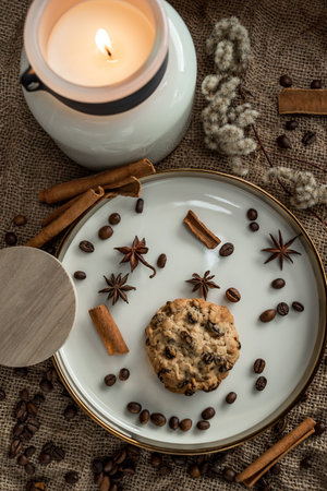 An elegant composition of candles, plates with a golden border, on which spices - anise, cinnamon and coffee beans lie. Against the background of burlapの写真素材