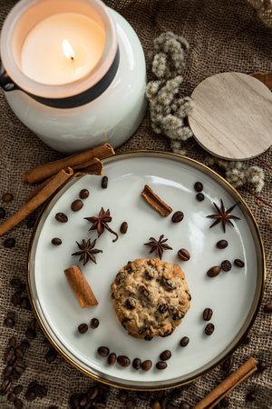 An elegant composition of candles, plates with a golden border, on which spices - anise, cinnamon and coffee beans lie. Against the background of burlapの写真素材