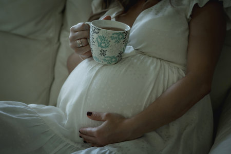 Pregnant woman drinks tea and rests on the couchの写真素材
