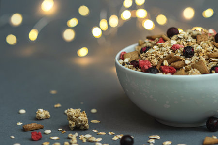 A bowl of muesli on a gray monochrome background with lights of garlands in the background, healthy food, healthy breakfastの写真素材