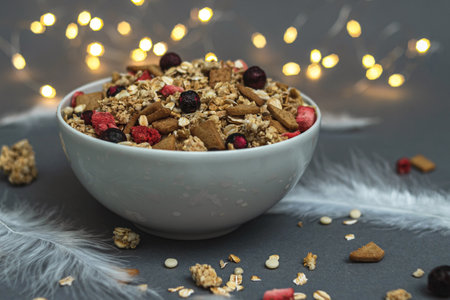 A bowl of muesli on a gray monochrome background, with white feathers and a side from a garland. Healthy food, healthy breakfastの写真素材