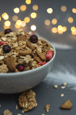 A bowl of muesli on a gray monochrome background, with white feathers and a side from a garland. Healthy food, healthy breakfastの写真素材