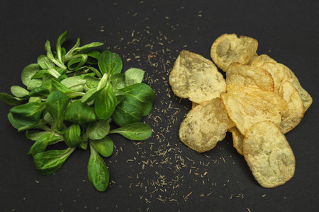 Lettuce leaves and chips on a black background. Healthy and unhealthy food is a contrast. Health care - the right choice of productsの写真素材