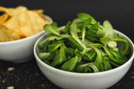 Two white bowls - one with green lettuce leaves, the second with chips, on a black background. Healthy food, health care, healthy lifestyleの写真素材