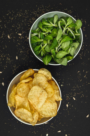 Two white bowls - one with green lettuce leaves, the second with chips, on a black background. Healthy food, health care, healthy lifestyleの写真素材