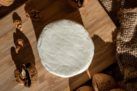 Composition of a round head of cheese with white mold and walnuts on a bamboo board on a background of burlapの写真素材