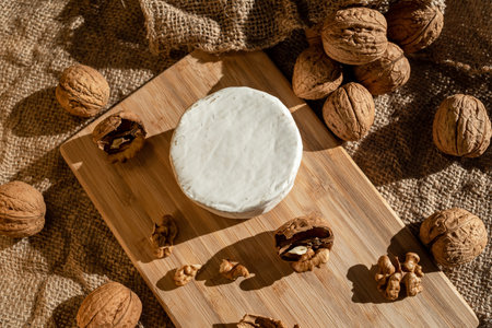 Composition of a round head of cheese with white mold and walnuts on a bamboo board on a background...