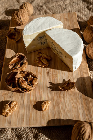 Composition of a cut cheese head with white and green mold and walnuts on a bamboo board on a background of burlapの写真素材
