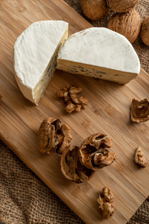 Composition of a cut cheese head with white and green mold and walnuts on a bamboo board on a...