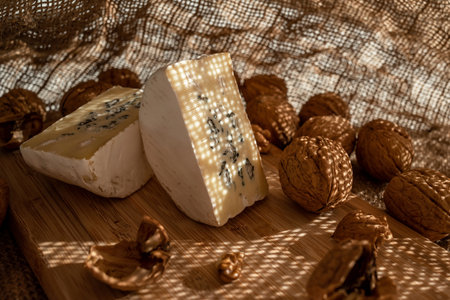Composition of a cut cheese head with white and green mold and walnuts on a bamboo board on a...
