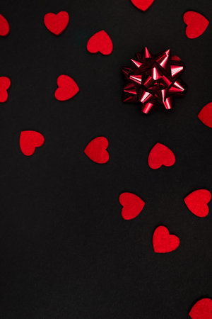 Black background decorated with small red hearts and a large red bow, with a place for the inscriptionの写真素材