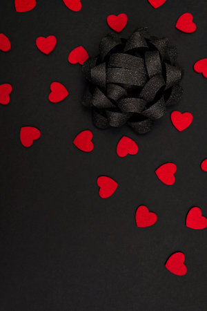 Black background decorated with small red hearts and a large black bow, with a place for the inscriptionの写真素材