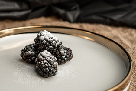 Blackberry berries and the reflection of light in a dish with a golden border. Light pattern on the plateの写真素材
