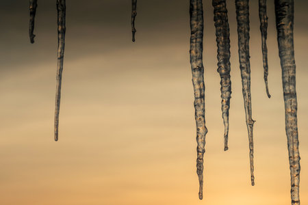 Beautiful long icicles hanging from the roof against the backdrop of a golden sunsetの写真素材