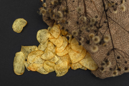 A canvas bag with potato chips scattered across a black table. Potato chips spilled out of bag
