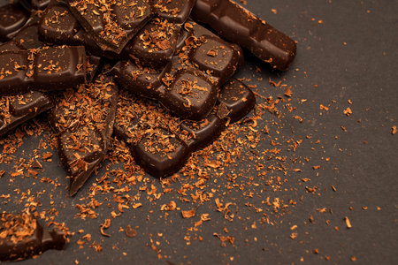<p>Pieces of dark and milk chocolate sprinkled with chocolate chips, on a dark background,...