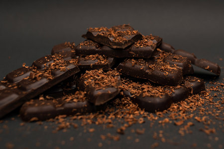 <p>Pieces of dark and milk chocolate sprinkled with chocolate chips, on a dark background,...