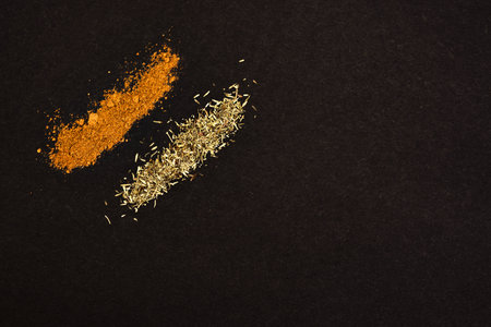Spices scattered on a black background. Coriander and rosemary heaped on a dark background.の写真素材