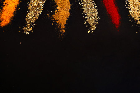 Spices scattered on a black background. Coriander, marjoram, paprika, thyme and rosemary, universal seasoning, garlic - heaped on a dark background.の写真素材