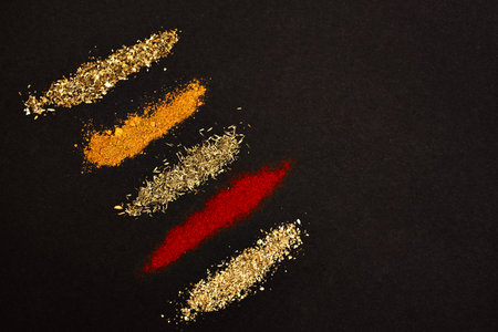 Spices scattered on a black background. Coriander, marjoram, paprika, thyme and rosemary, a universal seasoning, heaped on a dark background.の写真素材