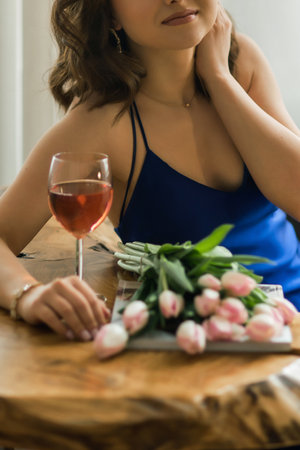 Young woman, in a blue dress, at a table with a bouquet of fresh flowers and a glass of rose wineの写真素材