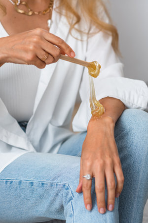 The hands of the beautician hold liquid sugar paste or wax for the duration of the depilation procedure in the salon. close up, background imageの写真素材