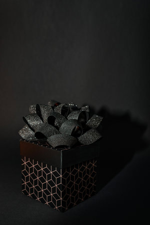 A black gift box with a geometric pattern and a black bow on a black background. Minimalist...