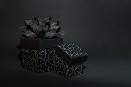 two black gift box with a geometric pattern and a black bow on a black background. Minimalist background for a holiday or discountsの写真素材