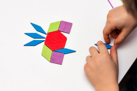 Close up of kid hands playing bright wooden tangram toy. The child collects a pattern of wooden...
