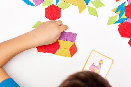 Close up of kid hands playing bright wooden tangram toy. The child collects a pattern of wooden...