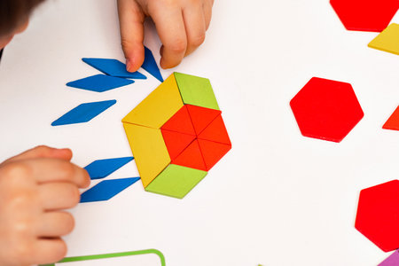 Close up of kid hands playing bright wooden tangram toy. The child collects a pattern of wooden...