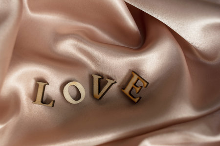 The inscription Love is made of wooden letters, on a background of pink draped silk fabric. inscription love background imageの写真素材