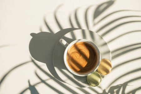 coffee cup, top view. fresh black morning coffee with macaroni on a white wooden table and plant shadows.の写真素材