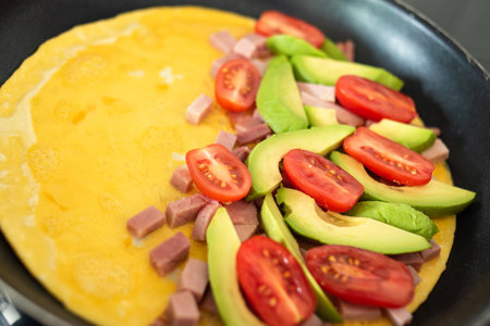 Omelette with ham, avocado and tomatoes in a frying pan